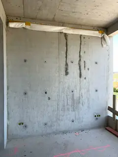 Sichtbetonwand mit zwei dunklen senkrechten Rissen unter einer Abdeckung, daneben Ankerlöcher