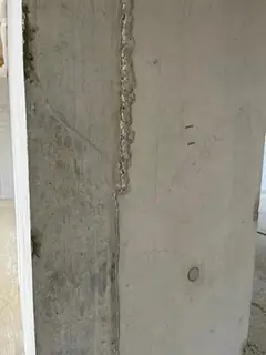 Senkrechte Schalungsfuge mit körnig ausgebrochener Kante, links eine weiße Holzleiste, rechts ein Ankerkonus