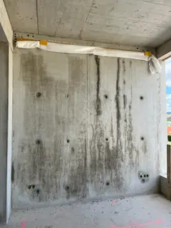 Raumecke mit Sichtbetonwand, dunkle senkrechte Läufer und Verfärbungen, oben eine weiße Abdeckung