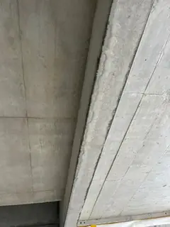Untersicht einer Betondecke mit diagonal verlaufendem Unterzug und feiner Fugenlinie, unten ein Gerüstrand