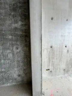 Betonstütze vor einer Sichtbetonwand mit Ankerlöchern, links ein dunklerer Wandabschnitt