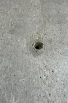 Kleines Spindelloch mit leicht ausgebrochenem Rand in einer Sichtbetonfläche mit feiner Maserung
