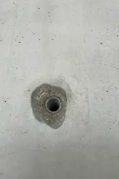 Spindelloch mit kleinem, dunklem Ausbruch am Rand, sonst glatte Betonfläche mit wenigen Lunkern
