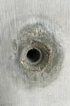 Spindelloch mit körnigem Ausbruch und dunklem Hof, im umgebenden Beton ist die Brettmaserung zu sehen