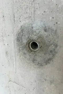 Spindelloch mit rundem, dunklem Hof und leicht beschädigtem Rand auf glatter Betonfläche