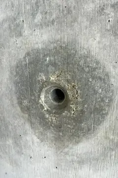 Spindelloch mit großem, dunklem Hof und kleinen Ausbrüchen am Rand, Betonfläche mit Brettstruktur