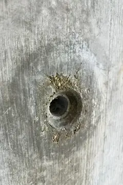 Spindelloch mit krümeligem, sandigem Ausbruch am oberen Rand und dunklem Hof in der Betonfläche