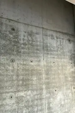 Sichtbetonwand mit senkrechter Fuge und Ankerlöchern, die Fläche ist leicht fleckig und wolkig