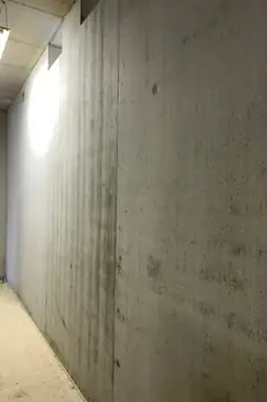 Langer Wandabschnitt aus Sichtbeton mit senkrechter Brettstruktur und dunklen Streifen, links ein Fenster