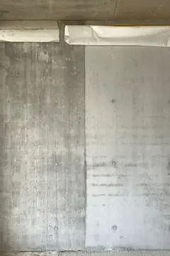 Zwei aneinanderstoßende Sichtbetonflächen, links dunkler, rechts heller, oben eine weiße Schutzabdeckung