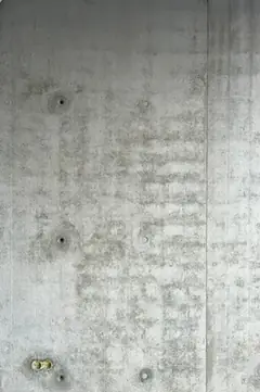 Sichtbetonwand mit wolkiger Oberfläche und mehreren Ankerlöchern, unten links zwei Elektrodosen