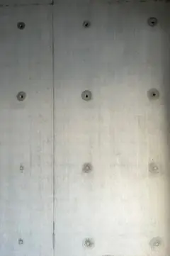 Gleichmäßiges Raster aus Ankerlöchern in einer hellen Sichtbetonwand mit einer senkrechten Fuge