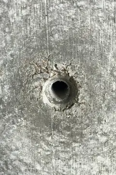 Spindelloch mit sternförmig auslaufenden feinen Rissen im Rand, umgeben von heller, fleckiger Betonfläche