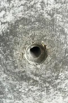 Spindelloch mit leicht ausgebrochenem Rand und feinem Mörtelrest, ringsum ein weicher dunkler Hof