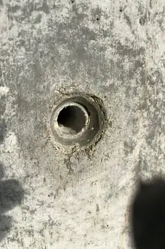 Größeres Spindelloch mit rauem, hellem Rand, rechts im Bild ein dunkler Schatten über der Betonfläche