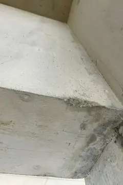 Betonbalken mit sichtbarer Brettmaserung an einer Gebäudeecke, darüber eine helle Wandfläche