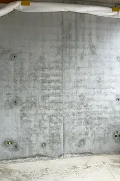 Sichtbetonwand mit Ankerlöchern und Elektrodosen am Wandfuß, oben eine weiße Schutzabdeckung