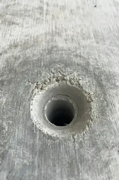 Tiefes, sauberes Spindelloch mit zackig ausgebrochenem Rand in einer fein gemaserten Betonfläche
