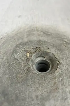 Spindelloch mit kleinen Rissen am Rand und breitem dunklem Hof, die Betonfläche ist oben heller