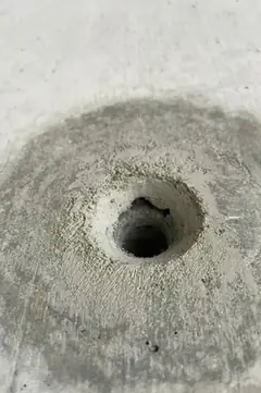 Spindelloch in einer rauen, hellen Mulde mit krümeligem Rand, ringsum ein großer dunkler Hof