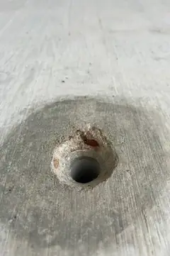 Spindelloch mit rostroter Verfärbung am Rand und großem, dunklem Hof auf glatter Betonfläche