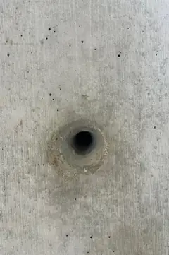 Kleines, sauberes Spindelloch mit schwach ausgeprägtem Rand in glatter Betonfläche mit wenigen Lunkern