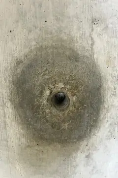 Sehr kleines Spindelloch in der Mitte eines großen, dunkelgrauen runden Hofs auf hellem Beton