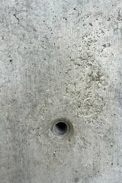 Kleines Spindelloch in einer Betonfläche mit körnigen, ausgemagerten Stellen und feinen Poren