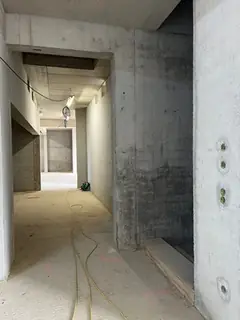 Langer Gang im Rohbau mit Sichtbetonwänden und Estrichboden, am Boden Kabel, rechts Ankerlöcher