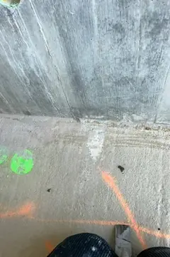 Wandfuß mit Estrichboden, grünen und orangen Farbmarkierungen, unten links ein Fuß im Schuh