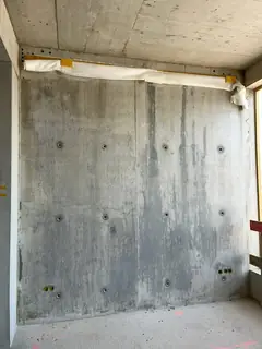 Sichtbetonwand mit breiten, dunklen Läufern in der Mitte, mehreren Ankerlöchern und Abdeckung am oberen Rand