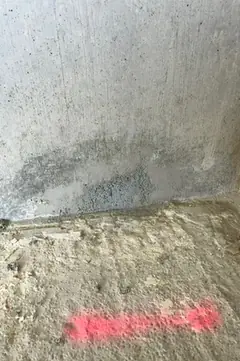 Wandfuß mit bläulich-grauer Stelle über einem rauen Estrichboden, am Boden eine rosa Markierung