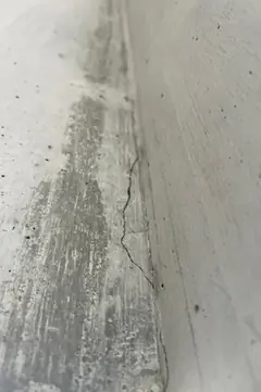 Feiner Riss an einer Betonkante, daneben ein grau verstrichener Streifen mit Spuren eines Pinsels