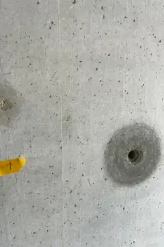 Spindelloch mit rundem dunklem Hof, links am Bildrand ein gelber Klebestreifen mit Pfeil