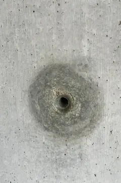 Kleines Spindelloch mit rundem Hof auf glatter Betonfläche mit einigen Poren, ohne größere Ausbrüche