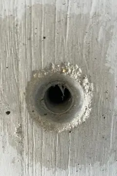 Spindelloch mit tiefer Öffnung und Ring aus grobem Sand, der Beton zeigt senkrechte Brettmaserung