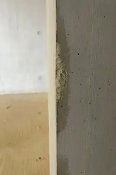 Betonkante neben einem Holzbrett, daran haftet ein körniger, heller Materialrest wie ein Kiesnest