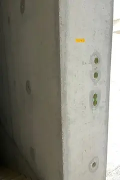 Betonstütze mit einer senkrechten Reihe kleiner Elektrodosen in ausgewaschenen Aussparungen, oben ein gelber Klebepunkt