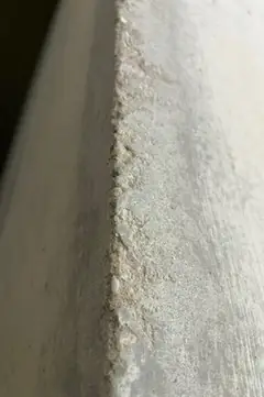 Betonkante mit gezackt ausgebrochenem Rand über die ganze Bildhöhe, links ein dunklerer Flächenanteil