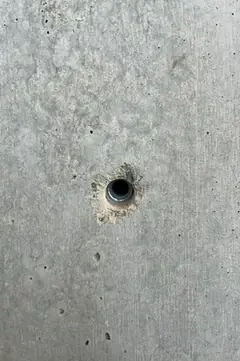 Spindelloch mit dunklem Kunststoffrohr und kleinem hellem Ausbruch am Rand, daneben feine Lunker