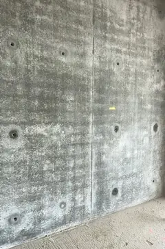 Sichtbetonwand mit Ankerlöchern, senkrechter Fuge und wolkiger Oberfläche, unten ein Estrichboden