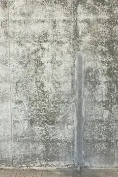 Sichtbetonwand mit senkrechtem, dunkelgrauem Streifen entlang einer Fuge und einem Ankerloch daneben