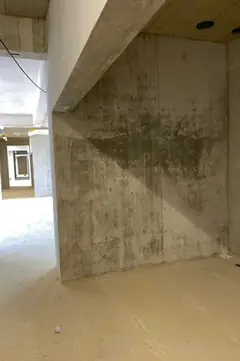 Raum im Rohbau mit Betonwand unter einem Unterzug, davor ein Estrichboden, links ein Durchgang
