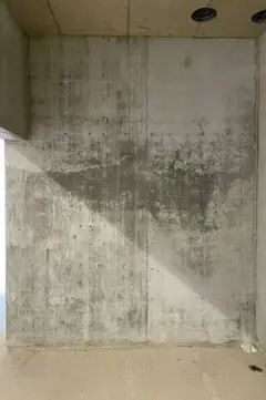 Sichtbetonwand mit Lichteinfall und dunklem Schattendreieck, oben Deckenöffnungen, unten ein Estrichboden