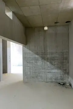 Rohbauraum mit Betonwand, Unterzug und Fensteröffnung, am Boden rechts etwas Schutt