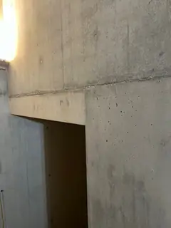 Betonwand mit Türöffnung und waagerechtem Unterzug, links fällt warmes Licht in den Raum