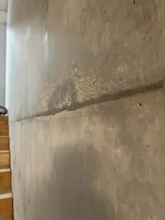 Waagerechte Betonierfuge an einer Wand neben einer Holztreppe, darüber eine raue, körnige Stelle