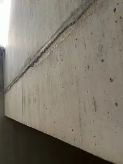 Diagonal verlaufende Fuge an einer Treppenwange aus Sichtbeton mit kleinen Lunkern, helles Licht oben links