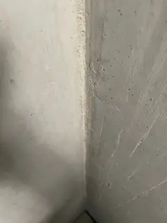 Innenecke zweier Betonwände mit feinen, strahlenförmigen weißen Kratzspuren auf der rechten Fläche