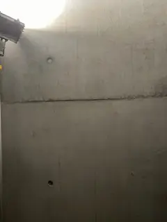 Dunkle Betonwand im Treppenhaus mit einem einzelnen Ankerloch, oben links fällt helles Licht ein